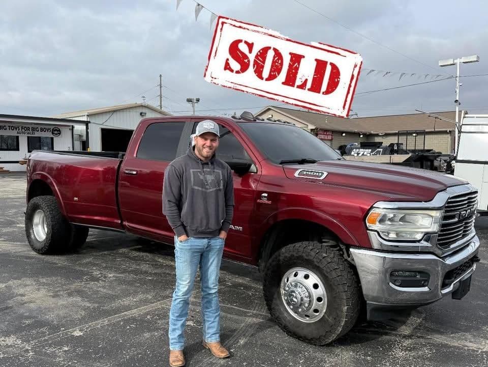 Man standing beside a sold red Dodge truck in a dealership lot.