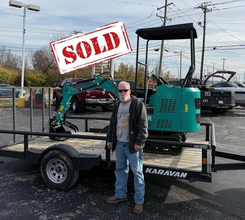 Man stands next to sold mini excavator on a trailer at a dealership.