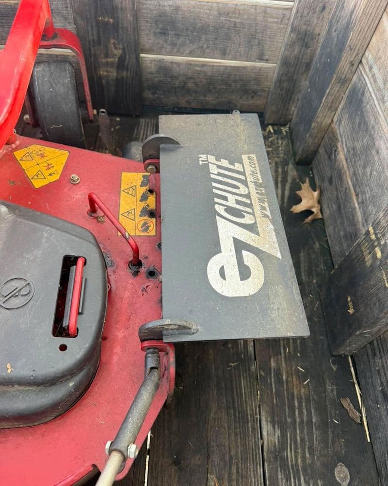 Close-up of a red lawn mower chute with safety warnings and "EZ Chute" branding.