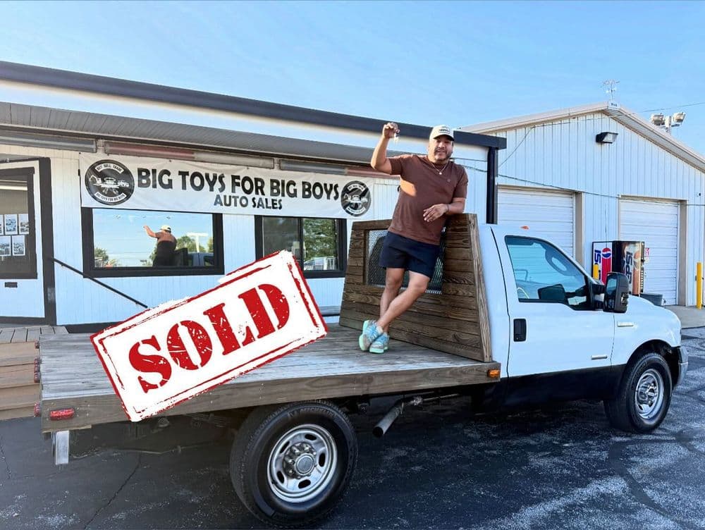 Man standing on a sold flatbed truck outside Big Toys for Big Boys Auto Sales.