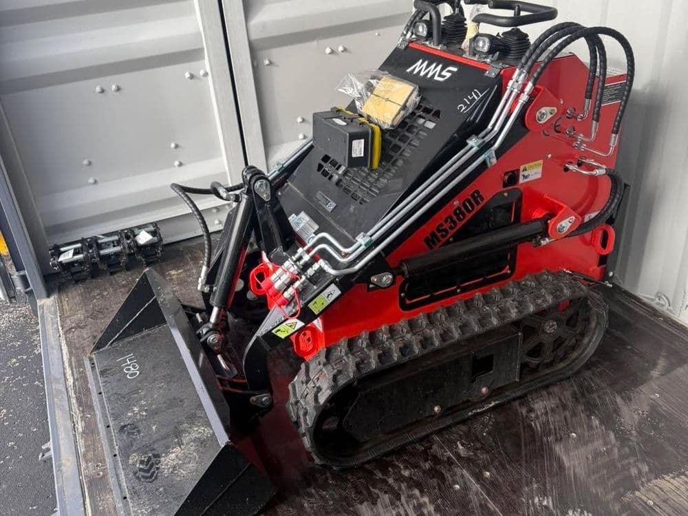 Compact track loader MS380R with attachments in shipping container, ready for transport.