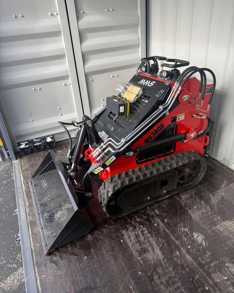 Compact tracked skid steer loader with attachments inside shipping container. Ideal for construction.