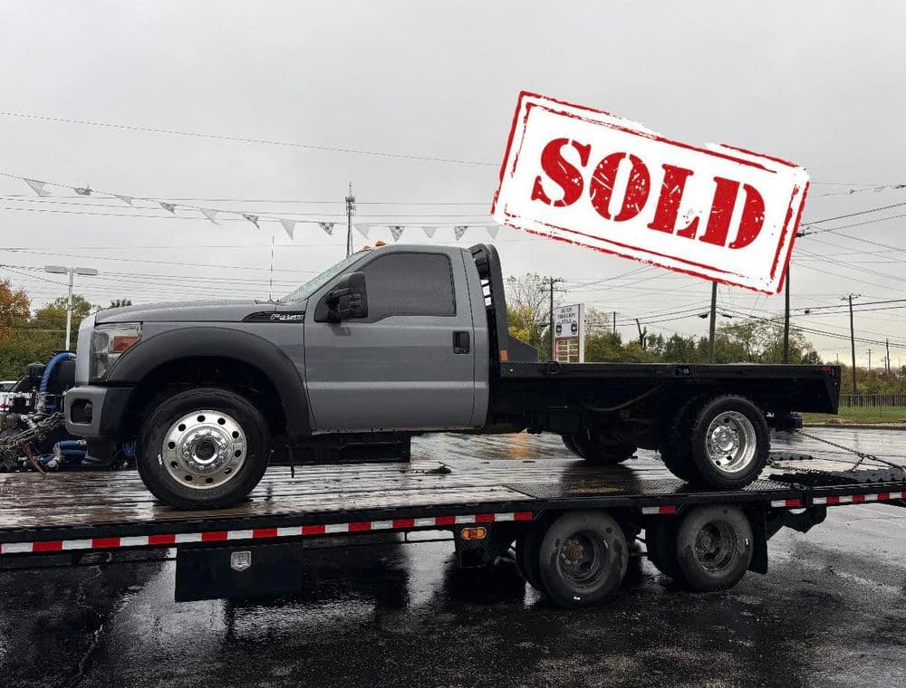 Gray Ford F-Series truck sold, displayed on a trailer with "SOLD" stamp overlay.