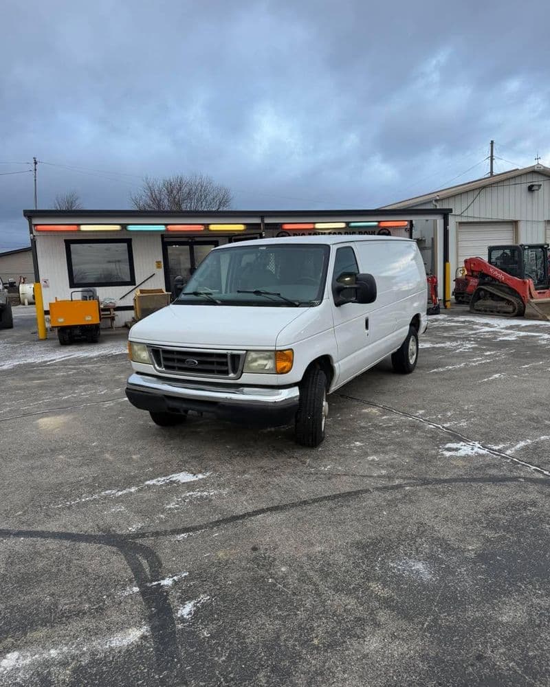 White cargo van parked on a paved surface near a building with colorful lights.