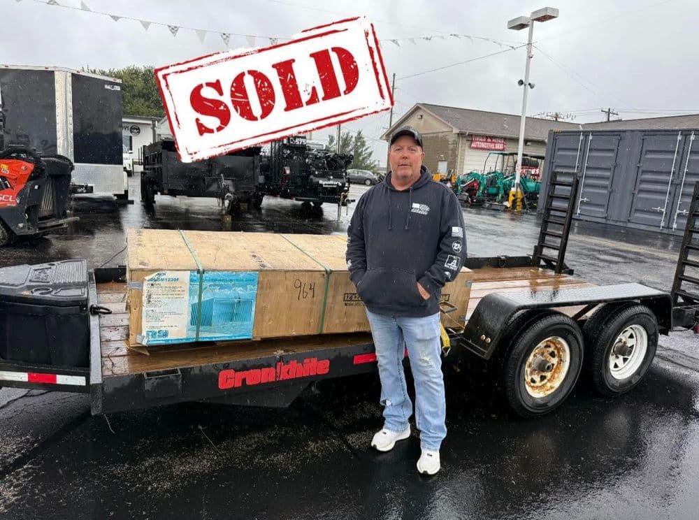 Man standing beside a sold trailer with a wooden pallet, featuring industrial equipment in background.