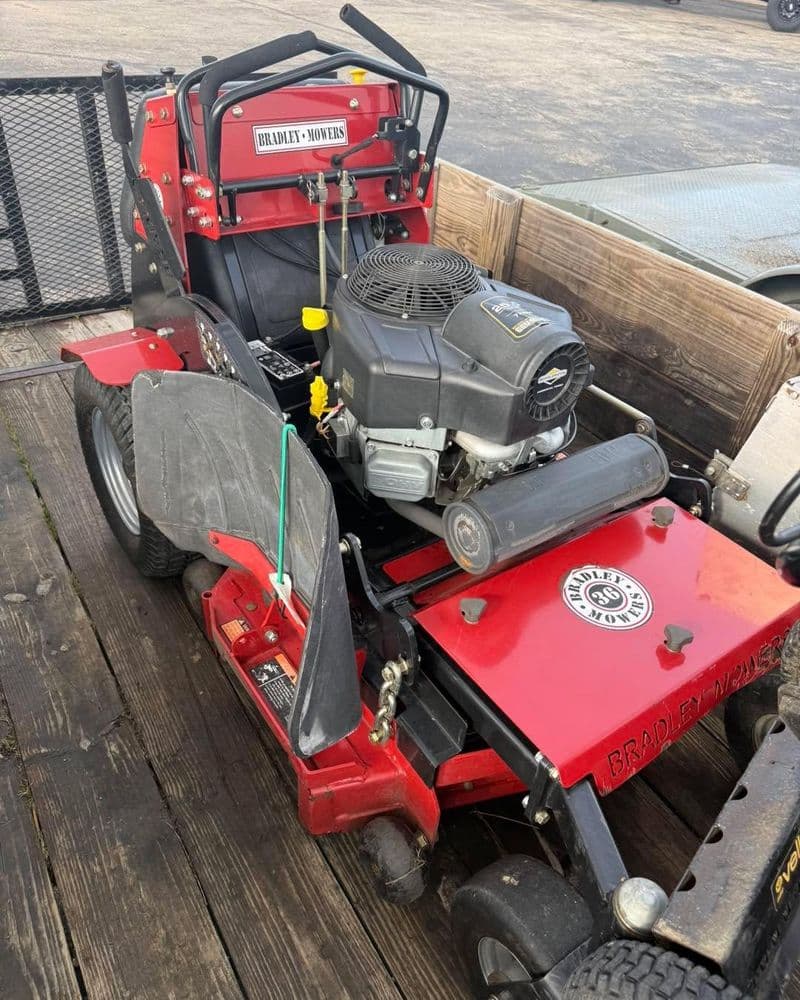 Red Bradley mower with a powerful engine, parked on a wooden trailer. Ideal for landscaping.