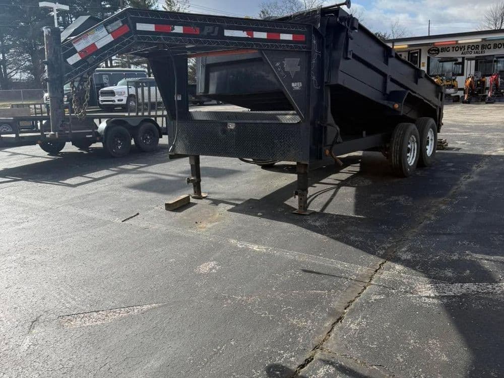 Black dump trailer parked on asphalt, showcasing its open loading area and sturdy wheels.