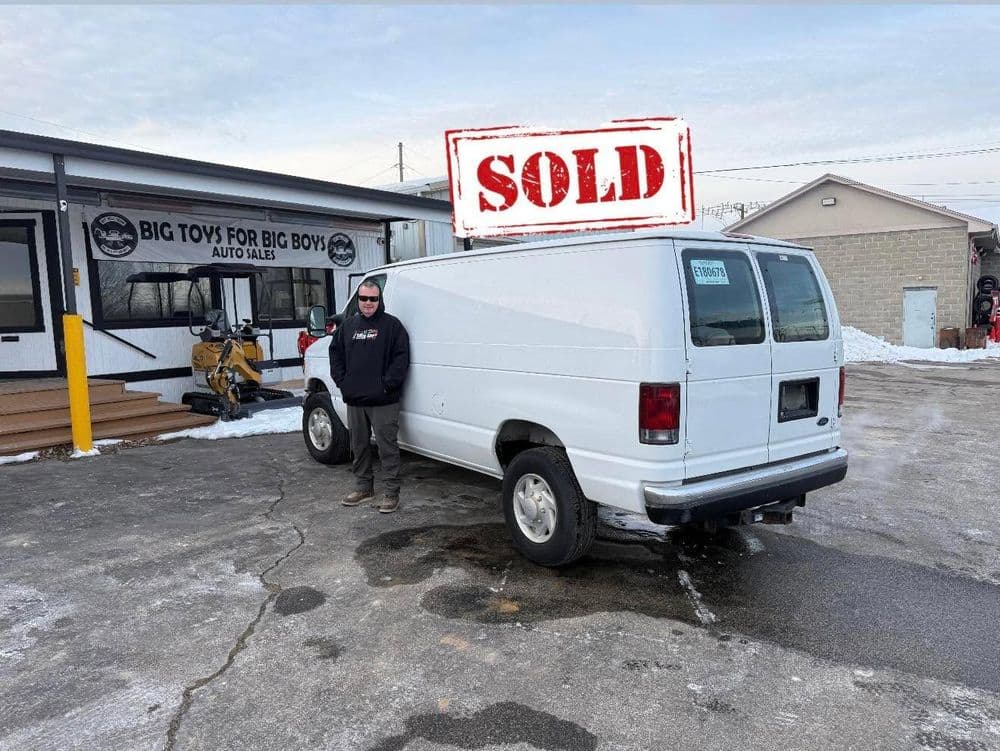White cargo van with "SOLD" stamp parked outside Big Toys for Big Boys Auto Sales.