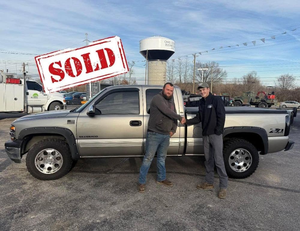 Sold pickup truck transaction with two men shaking hands by a silver Chevrolet Silverado.