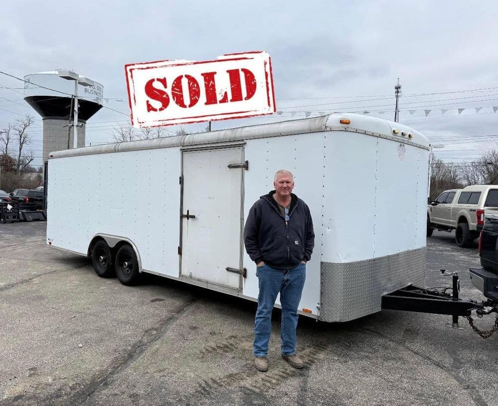 Man standing next to a sold trailer at a dealership with a water tower in the background.