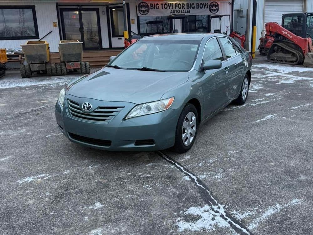 Toyota Camry parked outside an auto sale lot, showcasing its silver-blue exterior.