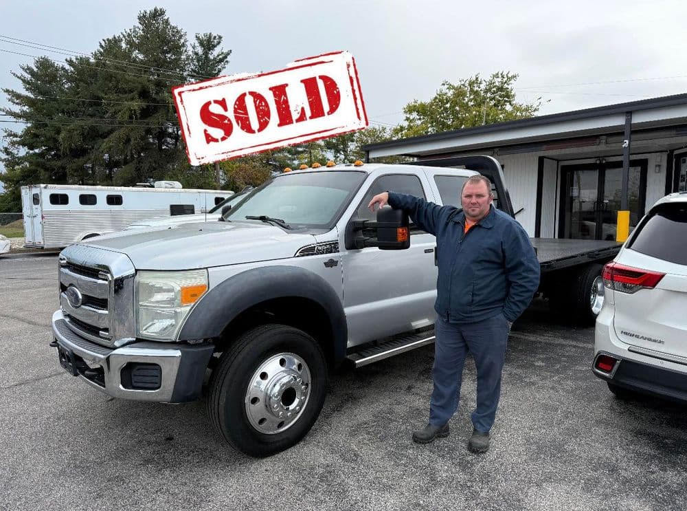 Man beside sold silver Ford F-250 truck at dealership with 'SOLD' stamp overlay.