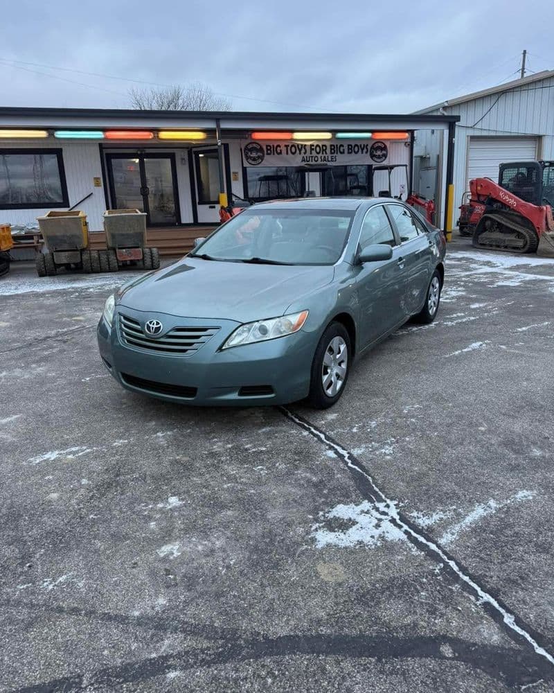 Toyota Camry parked outside an auto shop with snow on the ground, showcasing its modern design.