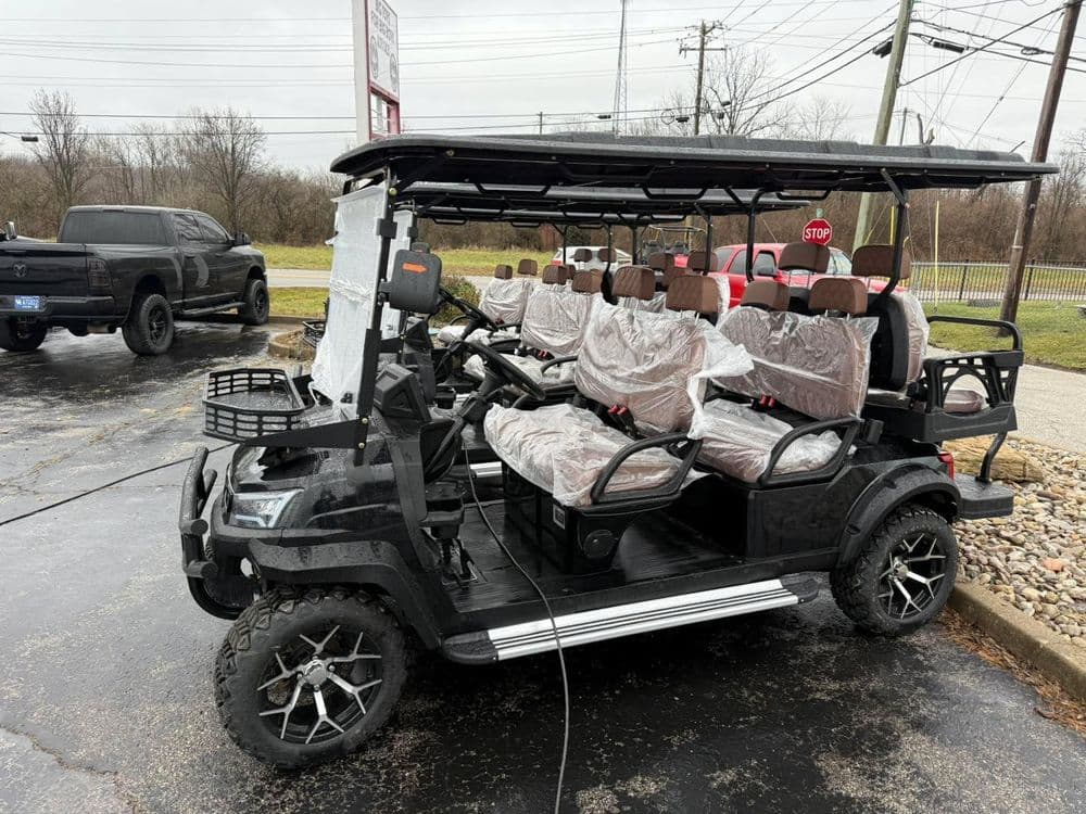 Black golf cart with covered seats, parked outdoors, near a sign and vehicles. Ideal for rentals.