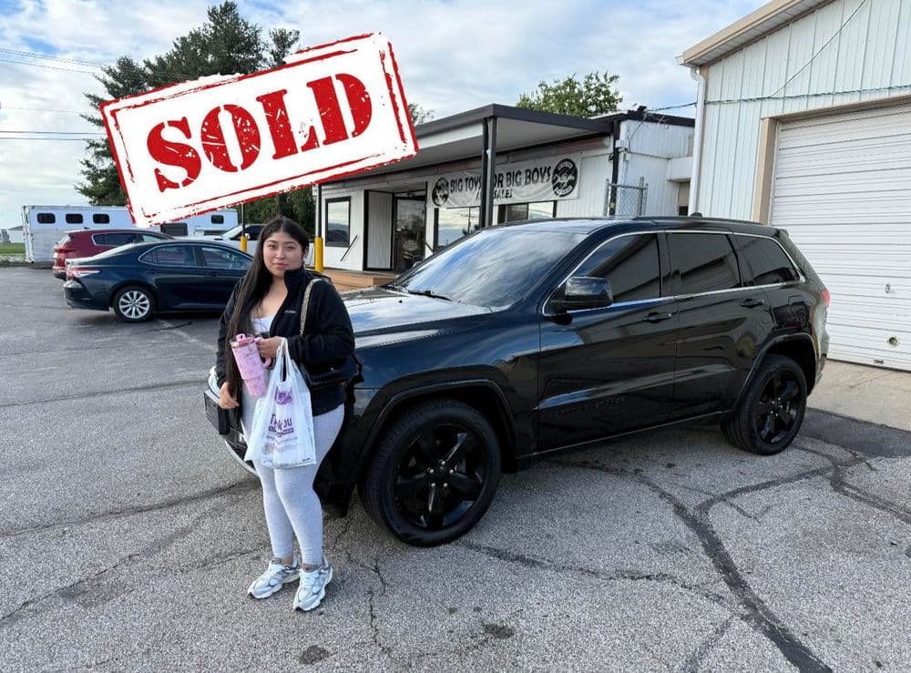 Young woman holding shopping bag stands by sold black SUV outside dealership.