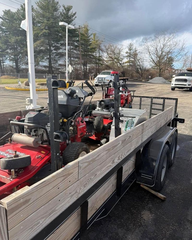 Landscape trailer loaded with lawn care equipment, including mowers and tools.