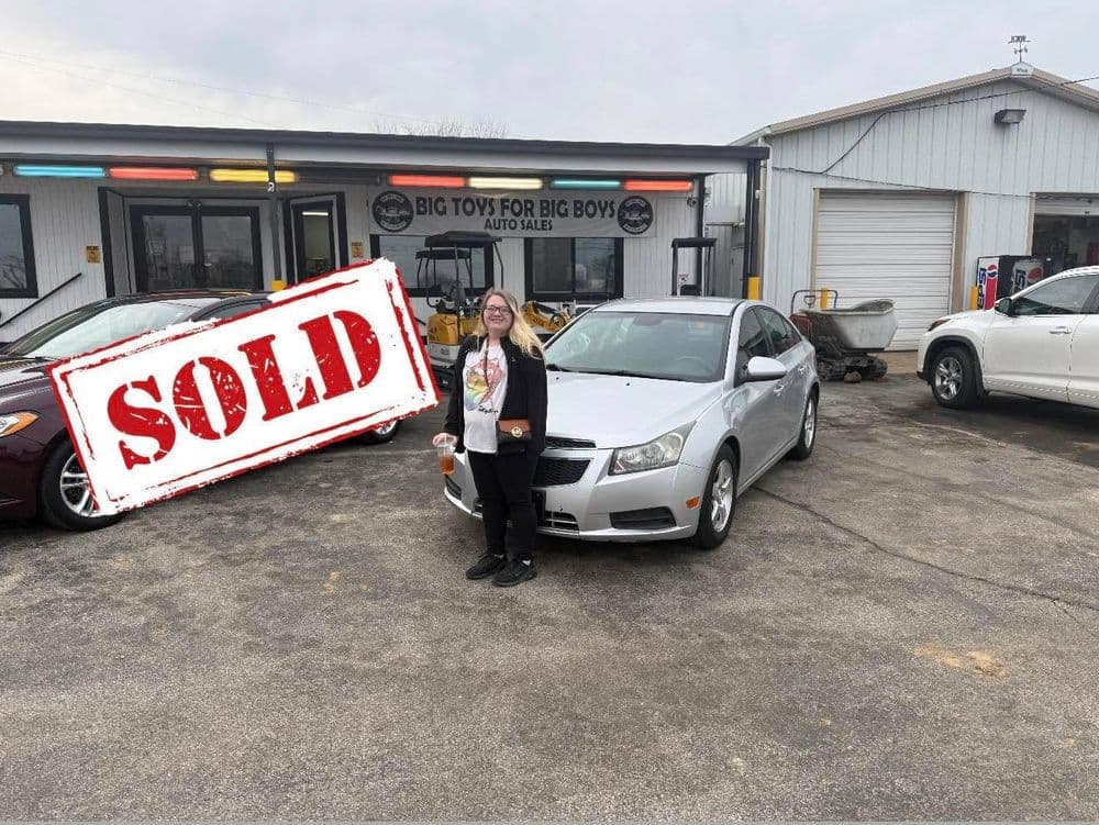 Happy customer stands next to sold silver car at Big Toys for Big Boys auto sales.