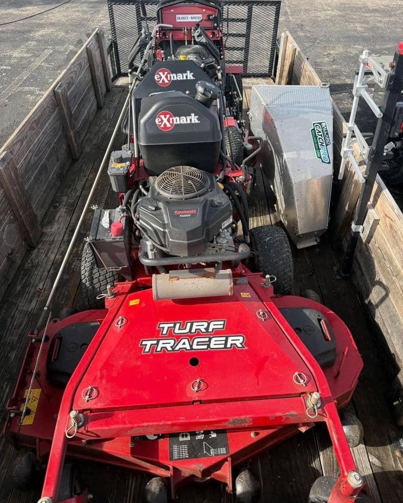 Red Exmark Turf Tracer mowers loaded on a trailer, ready for landscaping work.
