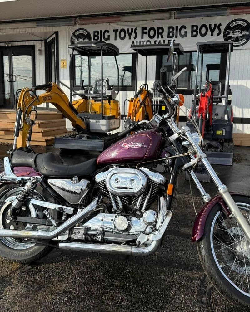 Motorcycle in front of auto sales with construction equipment and "Big Toys for Big Boys" sign.