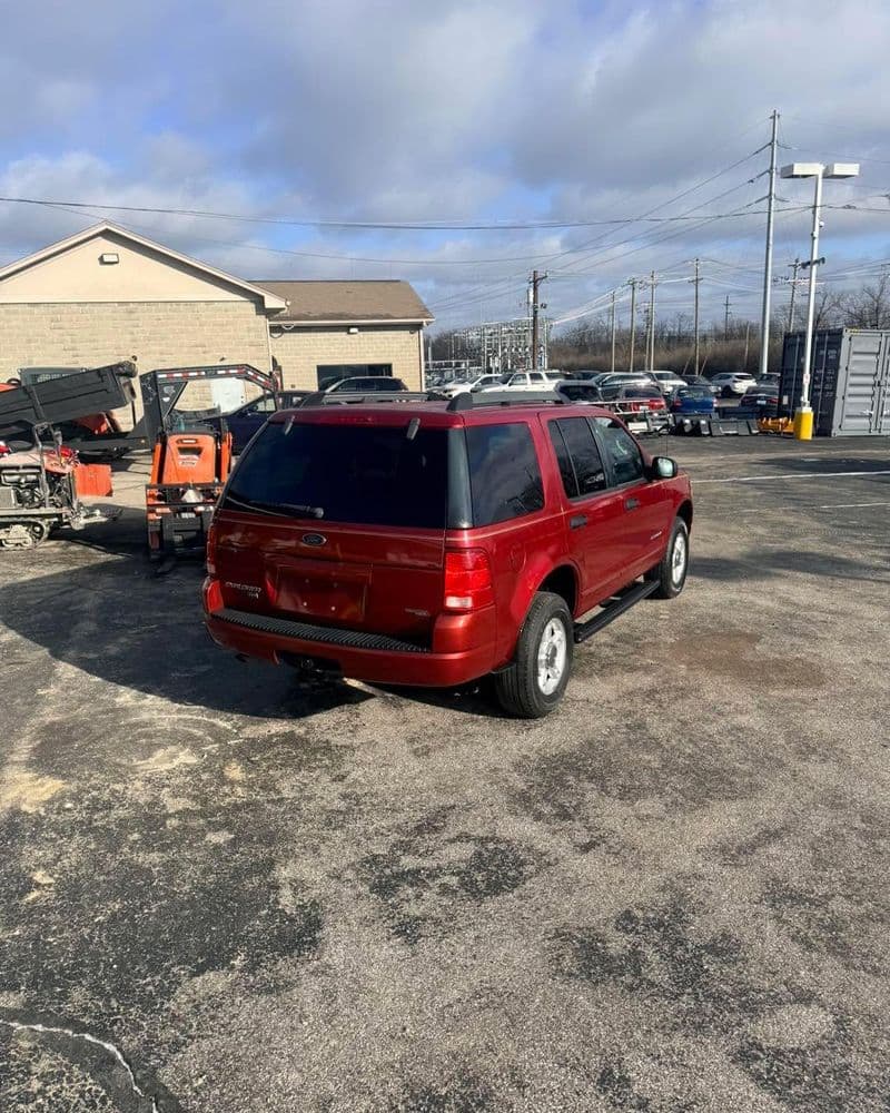 Red SUV parked in a used car lot with cloudy skies in the background.
