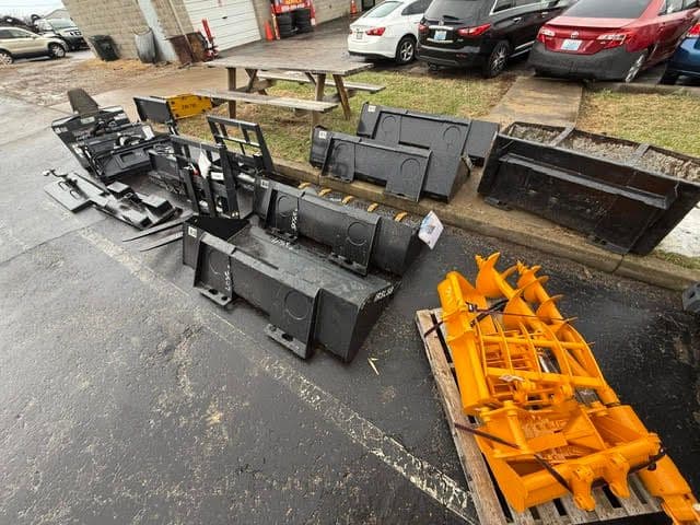 Various snow plow attachments in a parking lot for sale, showcasing different colors and designs.