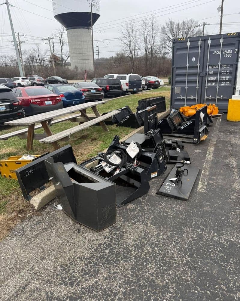 Row of discarded snow plow blades near a parking lot and shipping container.