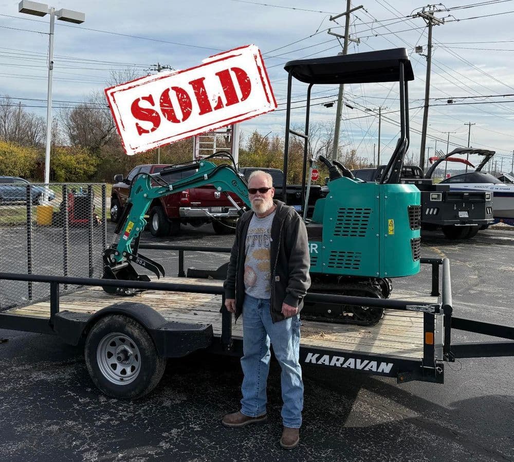 Man standing next to a sold mini excavator on a trailer, with a "SOLD" stamp over the image.