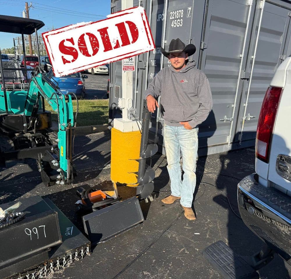Cowboy standing next to sold construction equipment at a dealership with a shipping container.