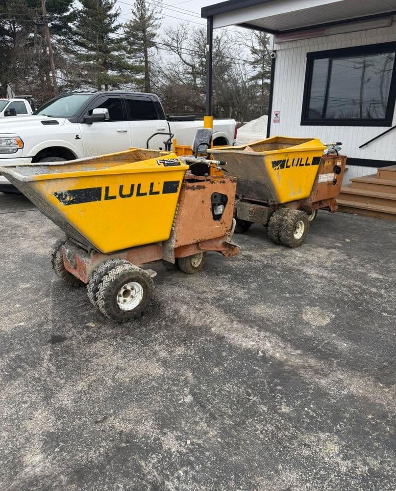 Two Lull brand construction dumpers parked outside a building on a gravel surface.