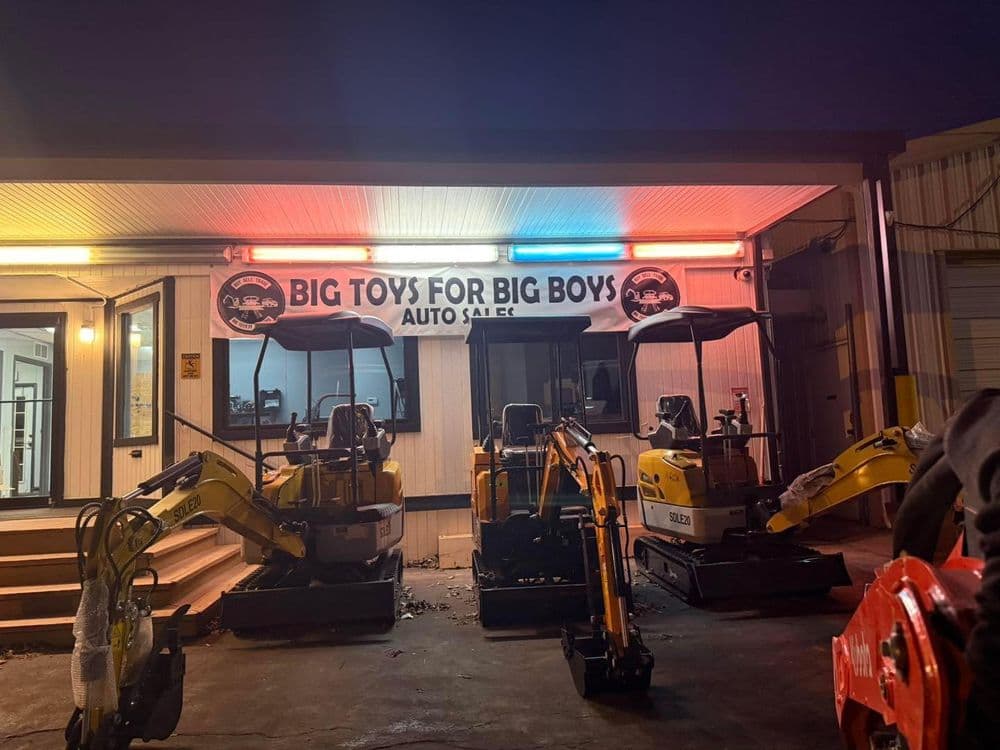 Excavators for sale at Big Toys for Big Boys Auto Sale, illuminated at night.