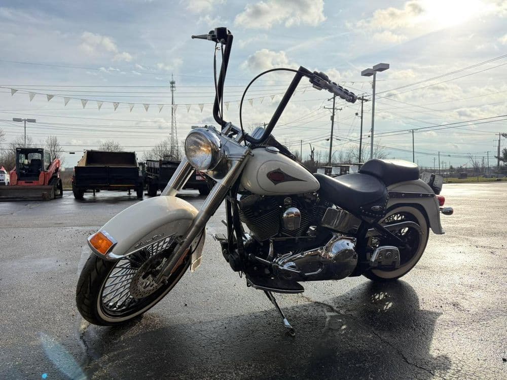 White custom motorcycle with extended handlebars parked on a reflective surface under a cloudy sky.
