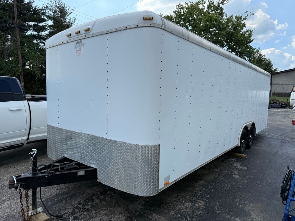 White enclosed trailer with a diamond plate hitch, parked in a lot, sunny day.
