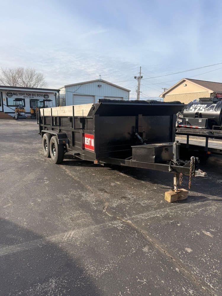 Black rental dump trailer parked in a paved lot with buildings in the background.