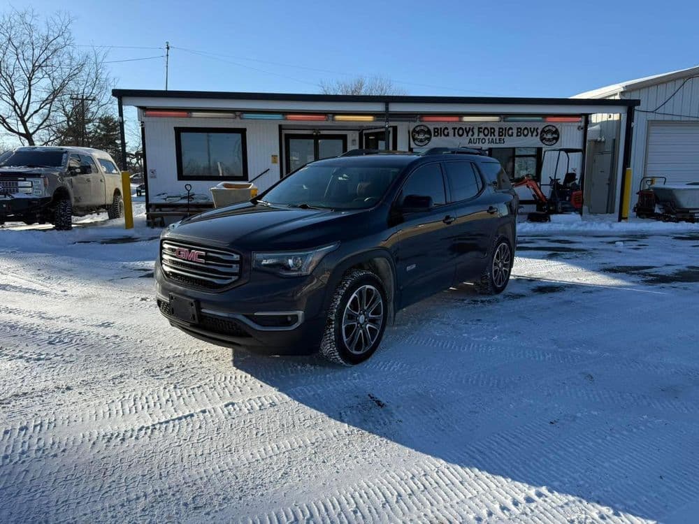 GMC Acadia parked in front of an auto shop on a snowy day with clear blue skies.