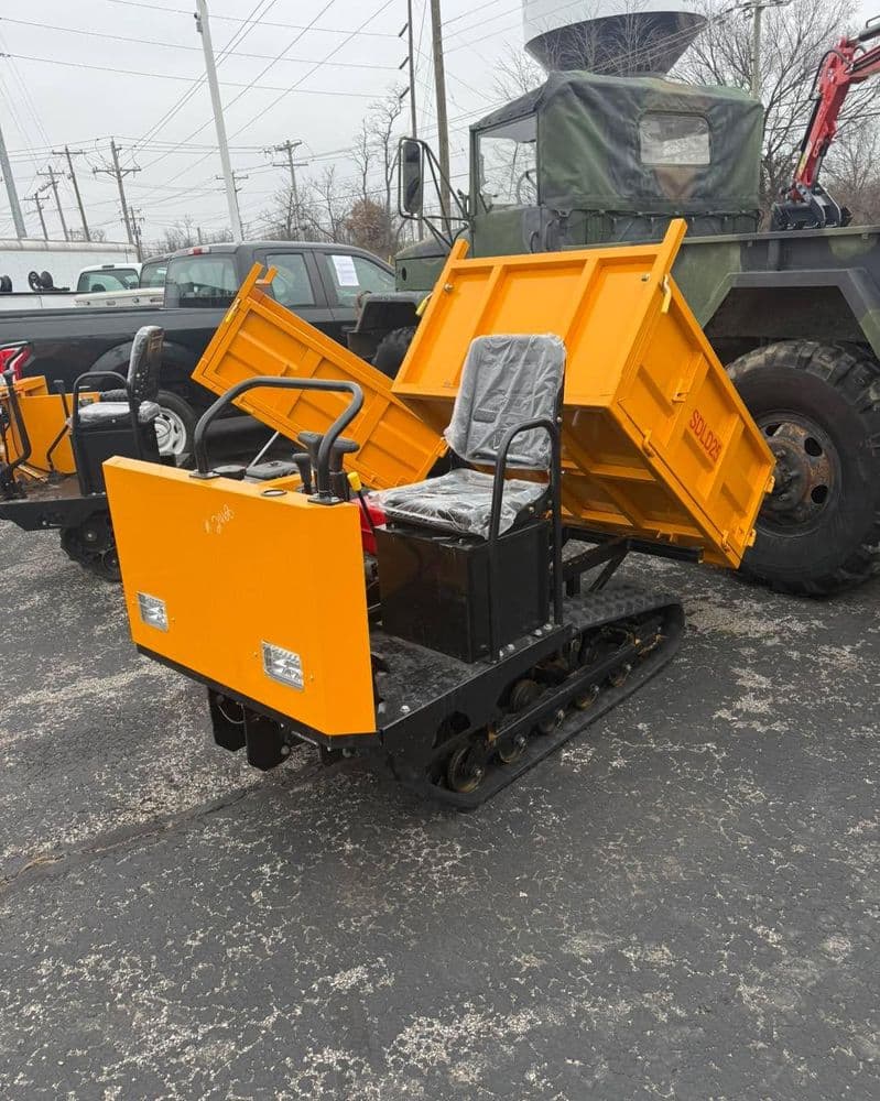 Compact orange tracked utility vehicle with a dump feature, positioned near a military truck.