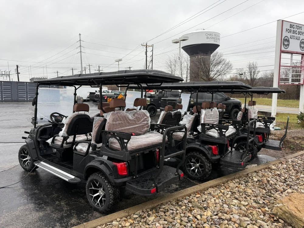 Four black golf carts with tan seats parked outside in a commercial area on a cloudy day.