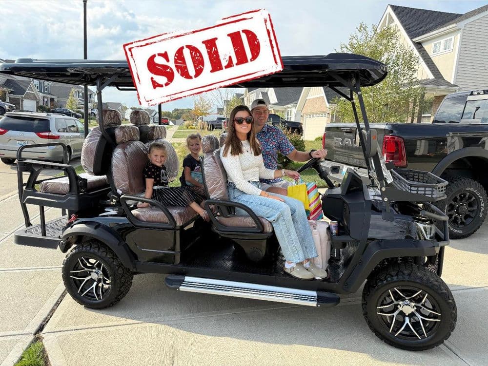 Family enjoying a sold black golf cart on a driveway, with kids and colorful bags.