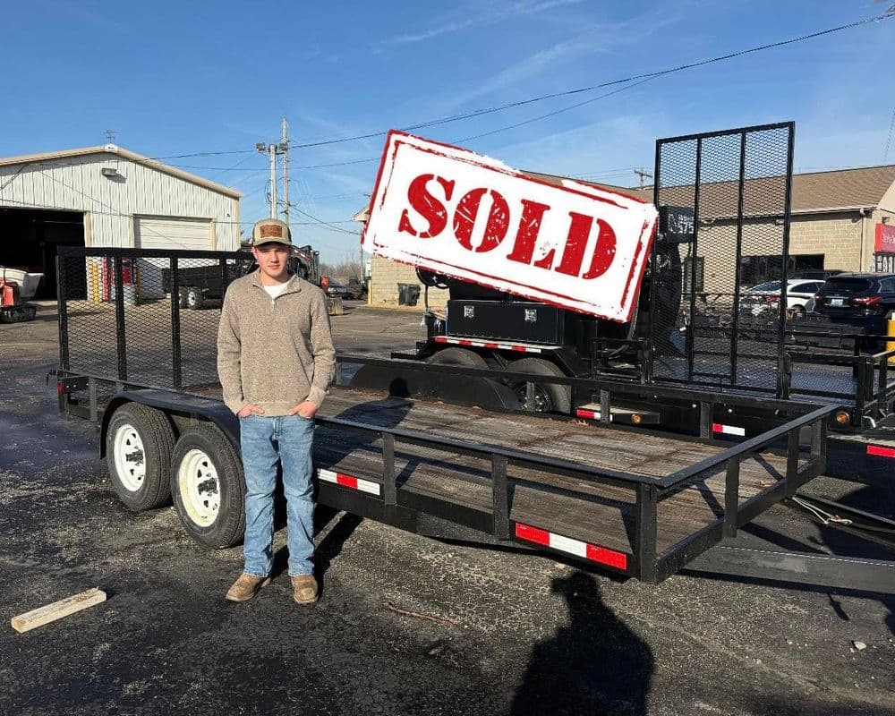 Young man standing beside a sold utility trailer in a commercial lot.