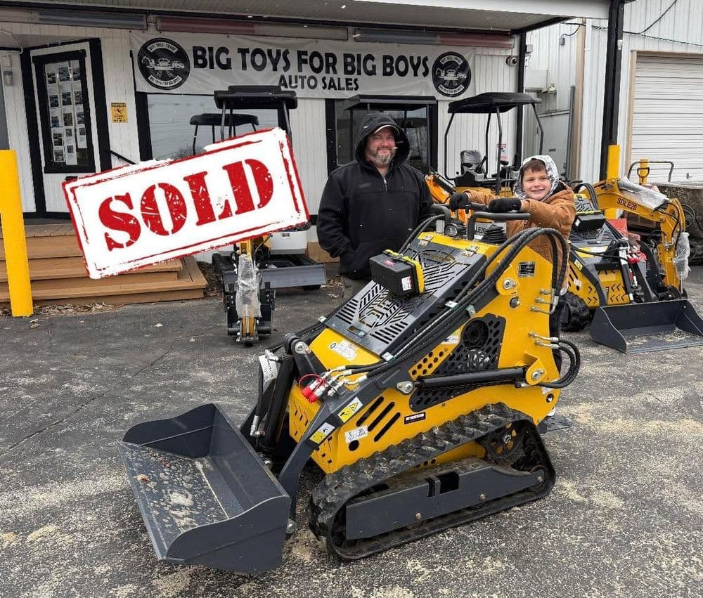 Man and boy stand by sold mini skid steer at Big Toys for Big Boys auto sales.