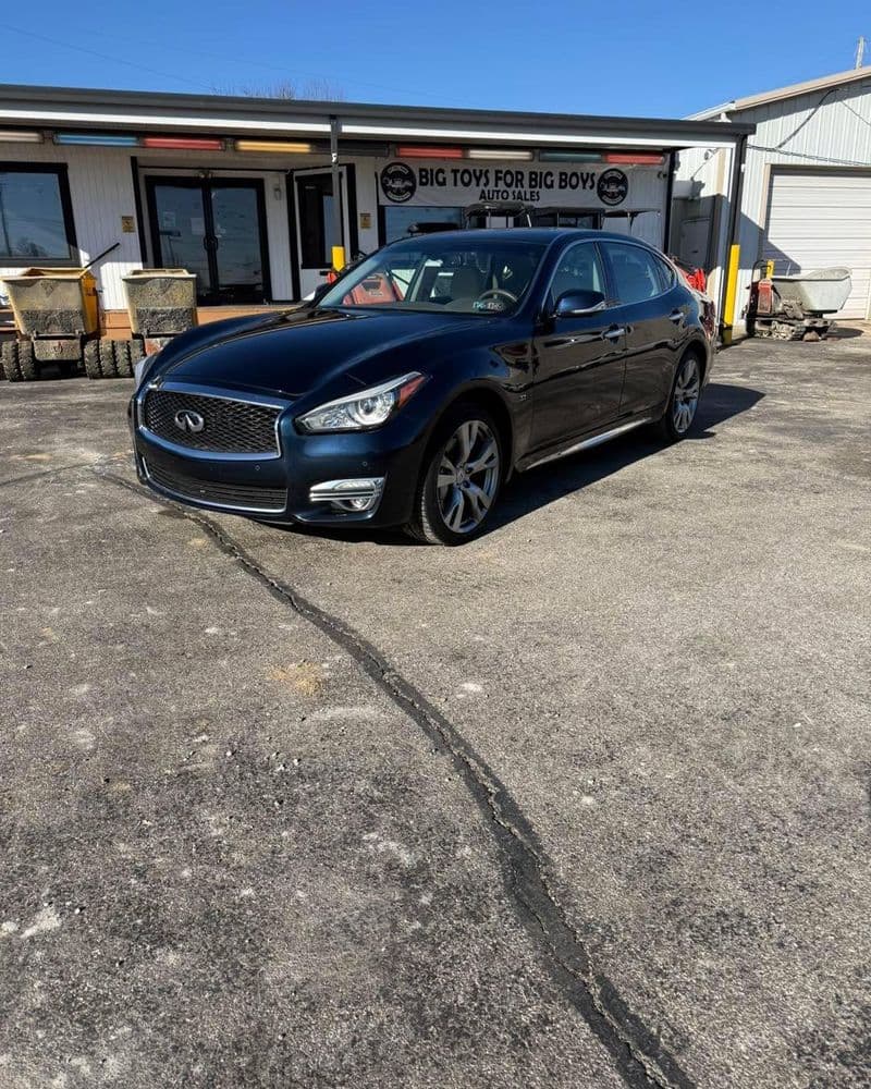 Black Infiniti Q70 parked outside a repair shop with clear blue sky and surroundings.